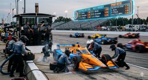 An IndyCar pit stop scene with crew members changing tires at high speed, blurred motion cars on track